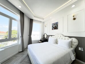 A hotel room with a large bed, a window with curtains, a wall-mounted light, and a painting. - Paris Hotel (Chau Doc)