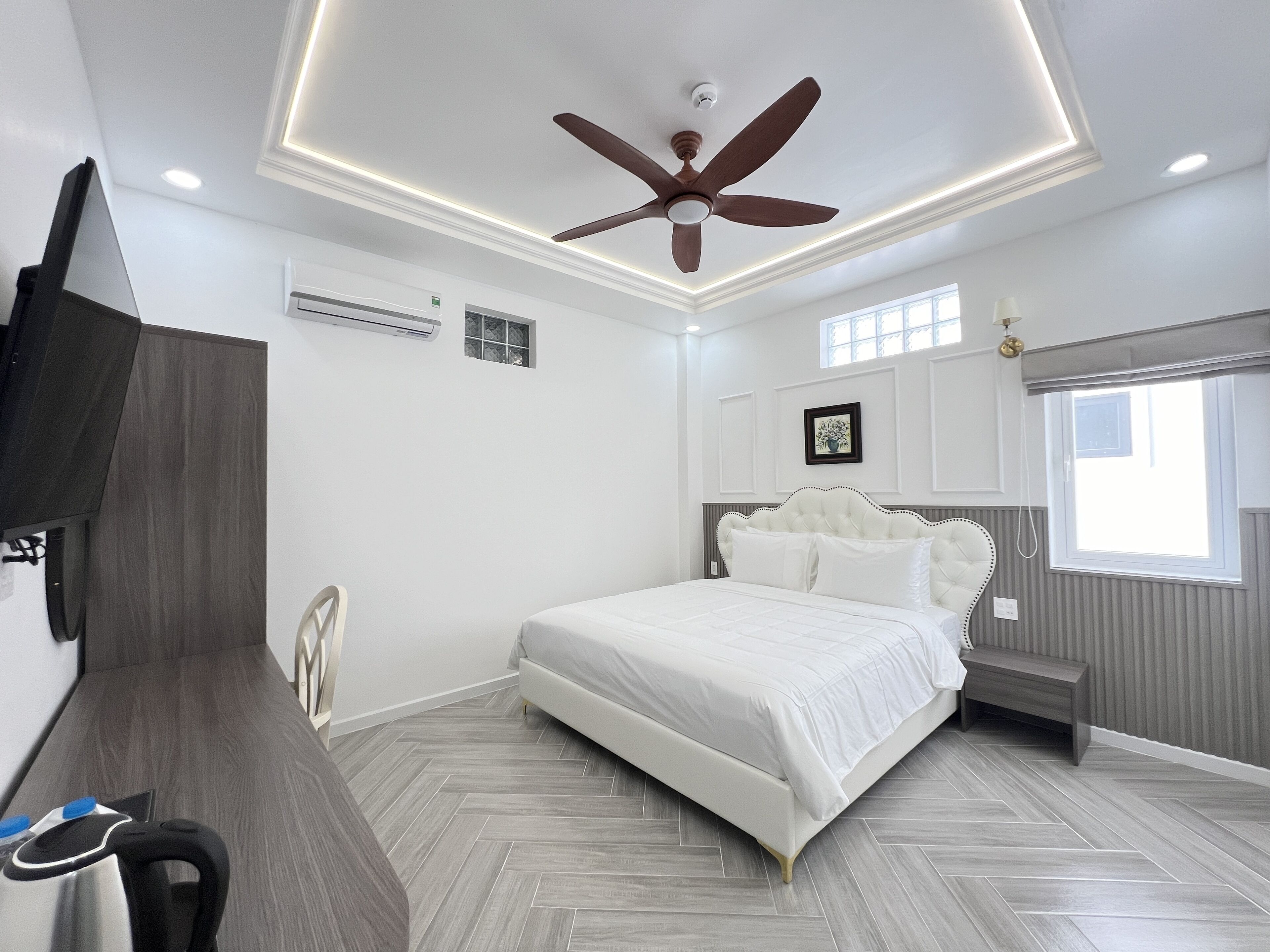 Ein Schlafzimmer mit einem Bett, einem Deckenventilator, einem Fernseher und einem Fenster.