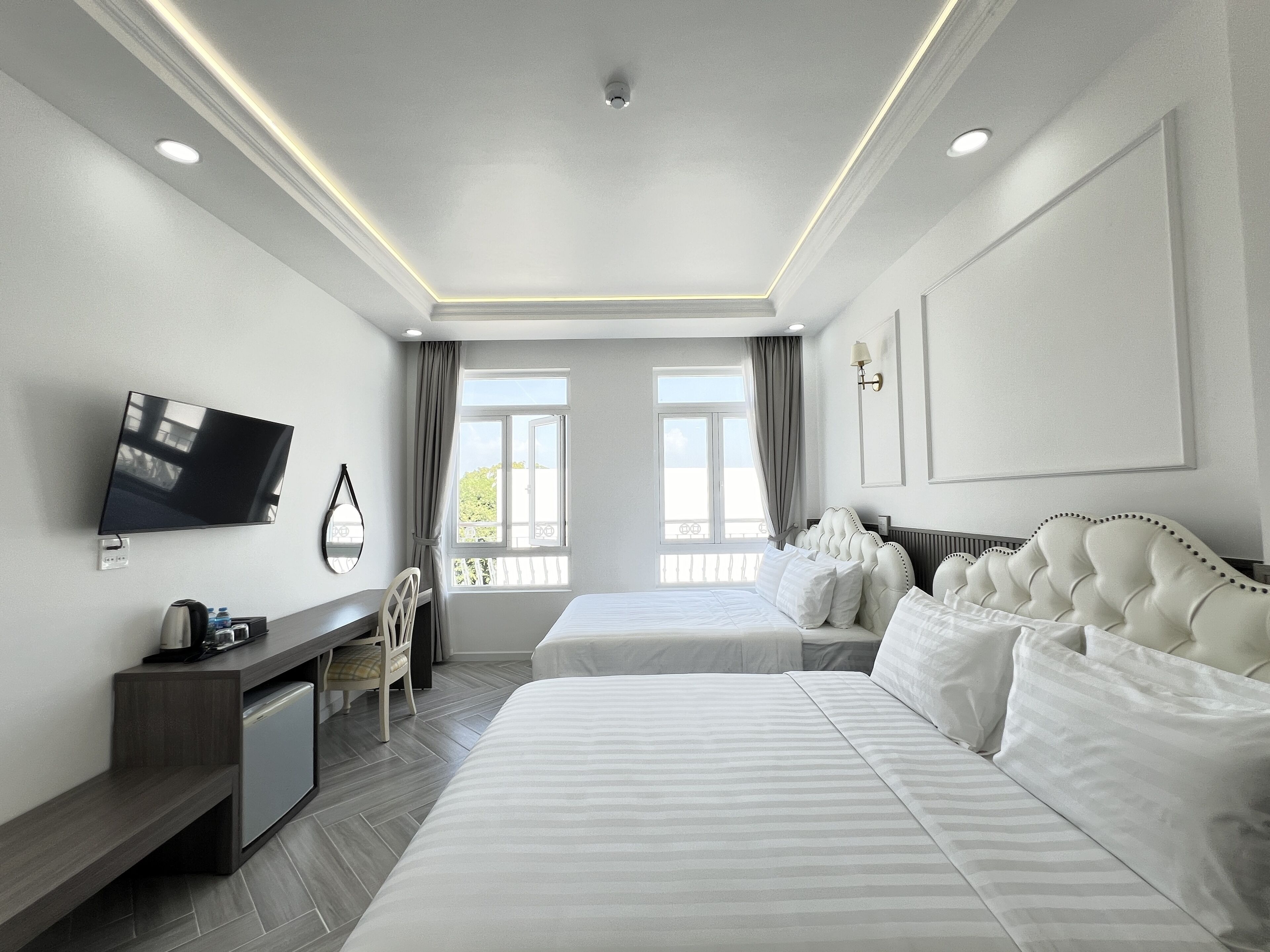 A hotel room with two beds, a desk, a TV, and a view of the outdoors.
