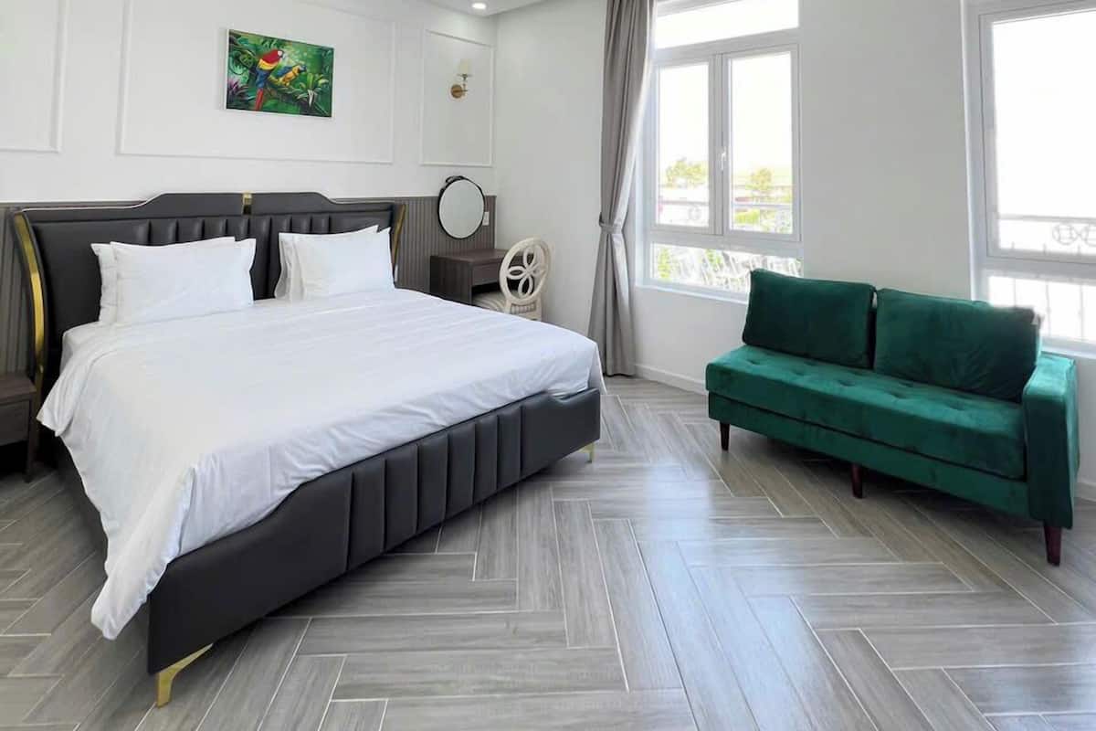 Un dormitorio moderno con una cama grande, un sofá verde y vistas al exterior a través de amplios ventanales.