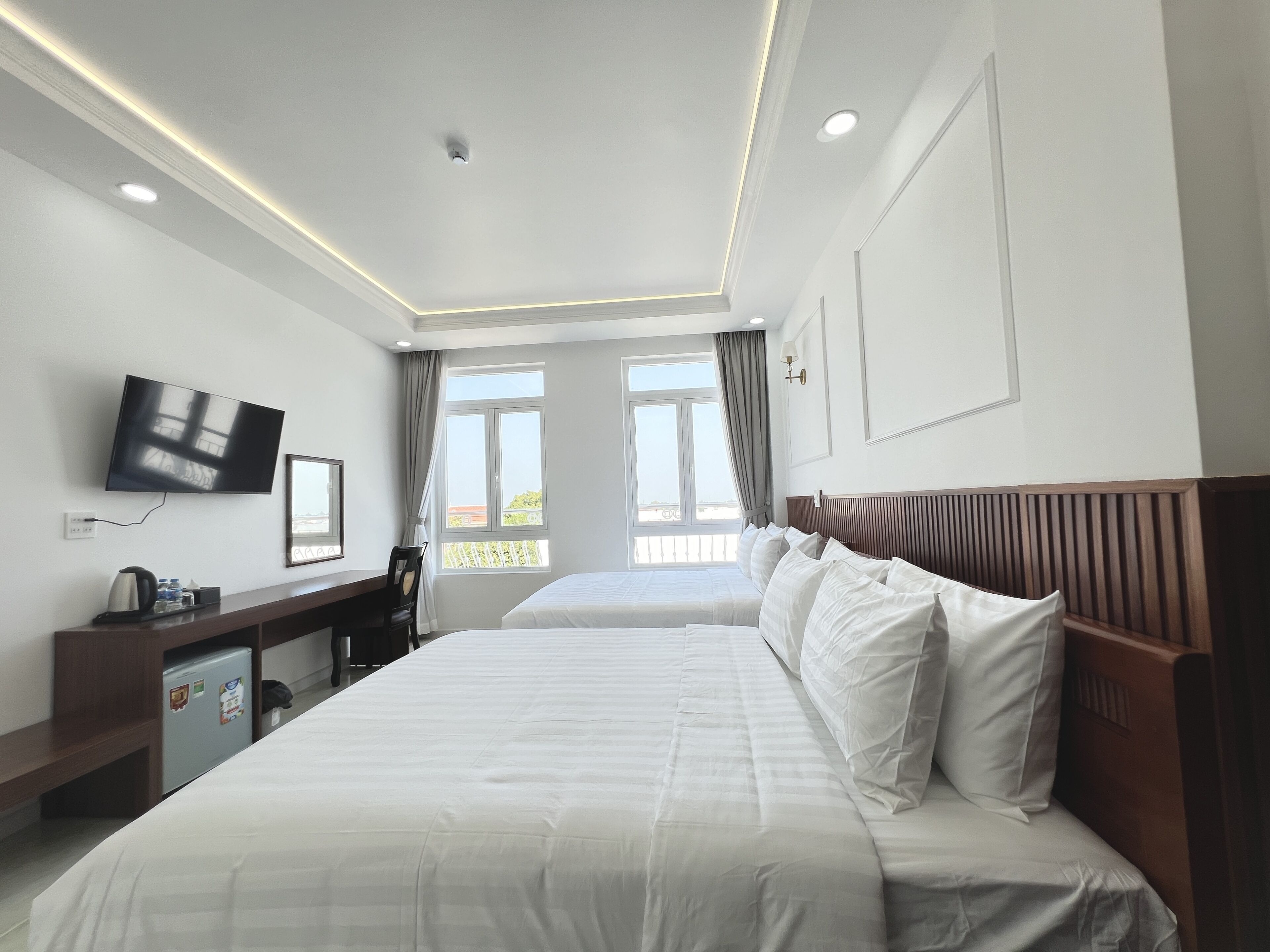 A hotel room with two beds, a desk with a chair, a television, and a window with curtains.