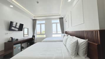 Quarto de hotel com duas camas, uma mesa de trabalho com cadeira, televisão e janela com cortinas.