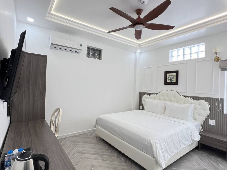 Un dormitorio moderno con cama, ventilador de techo, televisor montado en la pared y un escritorio de madera con hervidor.