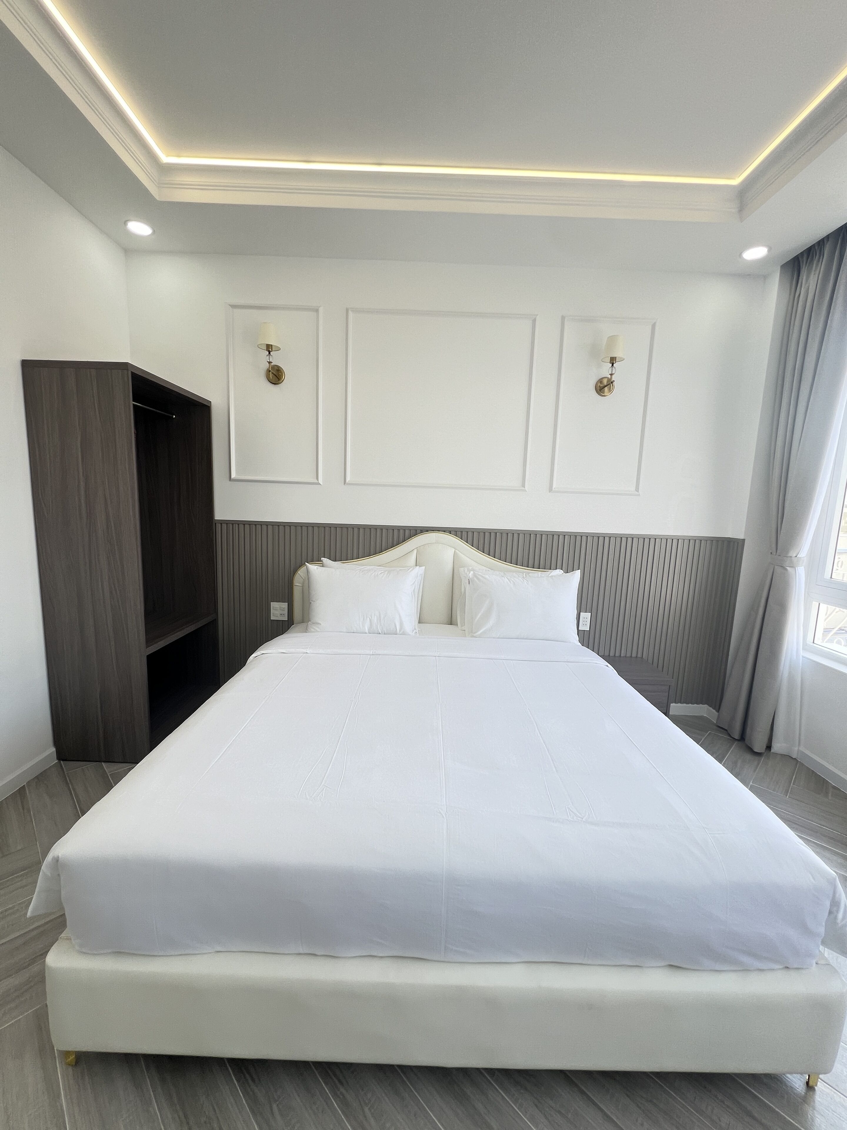 A large, neatly made bed in a modern hotel room with a built-in wardrobe and a large window with curtains.