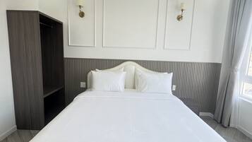 A large, neatly made bed in a modern hotel room with a built-in wardrobe and a large window with curtains.