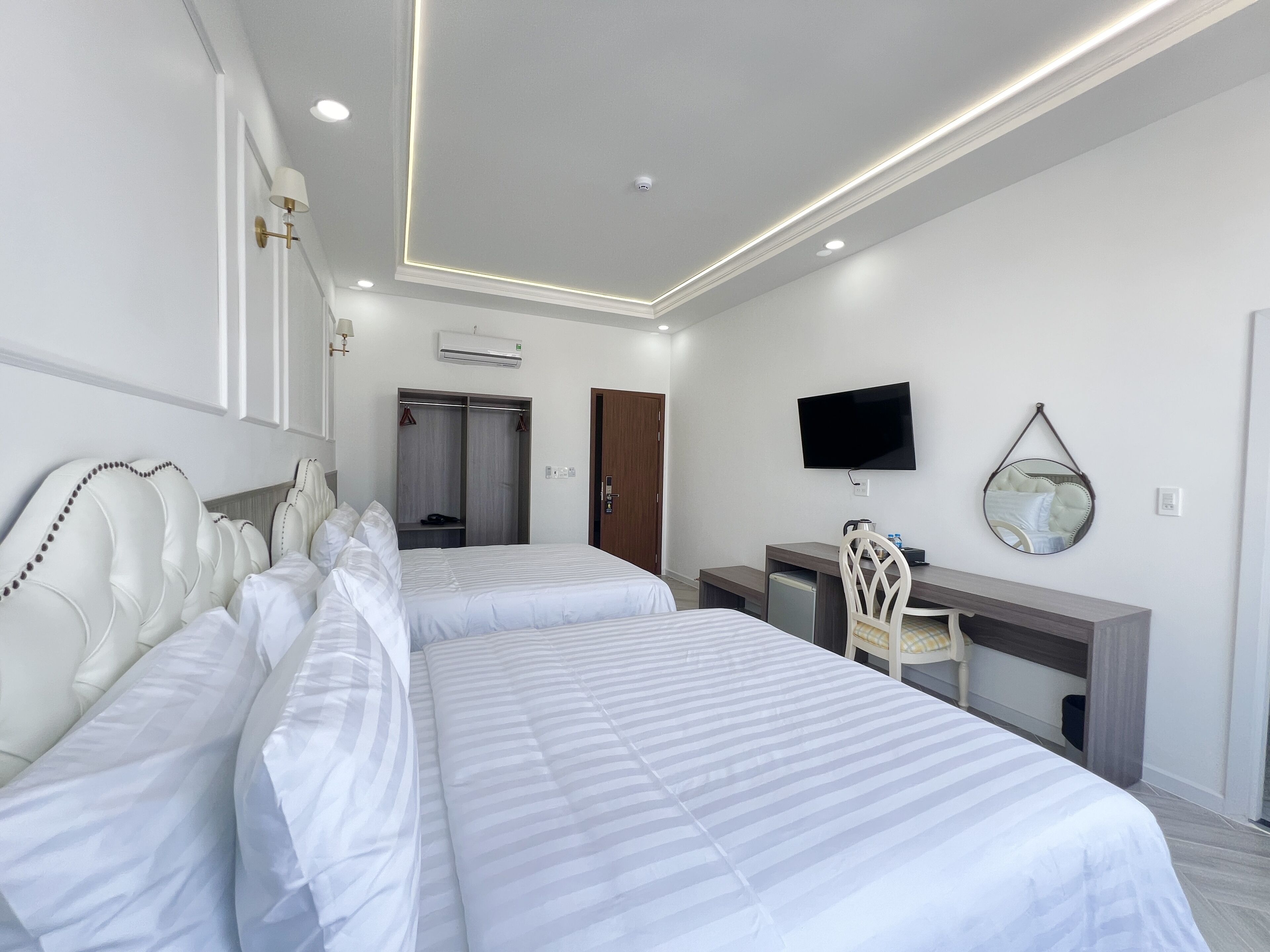 A hotel room with two beds, a desk, a chair, a TV, and a mirror.