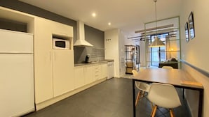 Una cocina moderna con armarios blancos, una zona de comedor con mesa y sillas, y vistas al salón a través de una pared de vidrio.