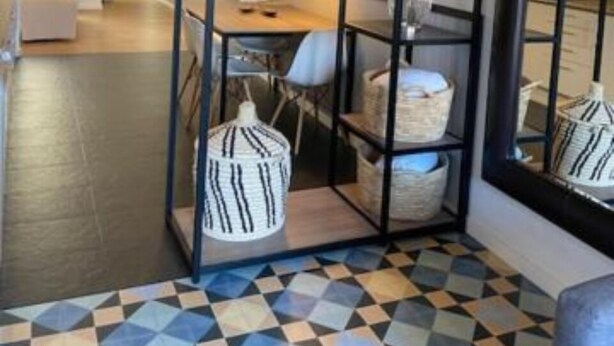 Una habitación con piso de estampado geométrico, un estante de metal negro con cestas y un espejo grande que refleja la habitación.