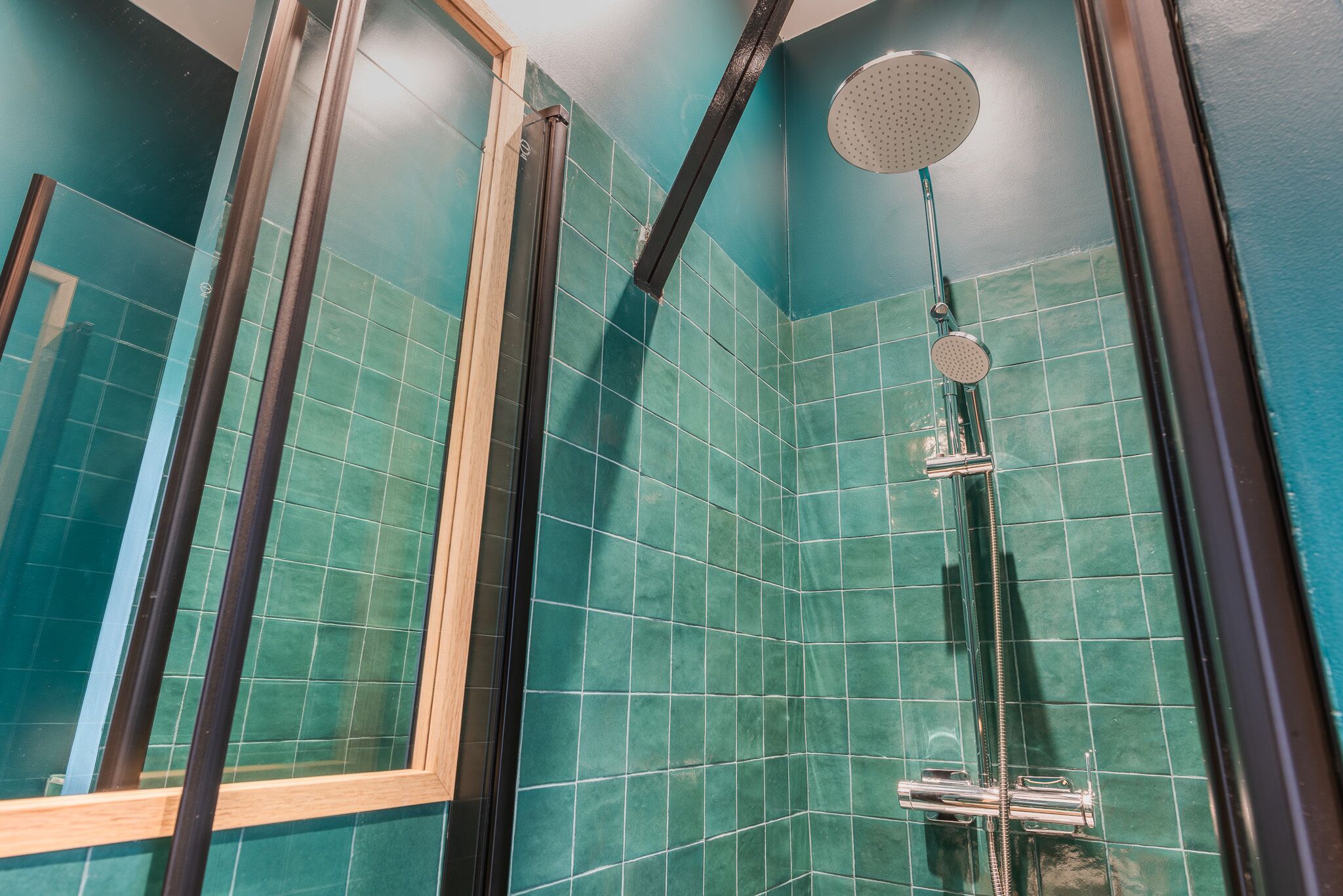 A corner of a bathroom with teal tiles, a glass shower enclosure, and a showerhead.