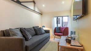 A living room with a sofa, a coffee table, a TV mounted on the wall, and a window with curtains.
