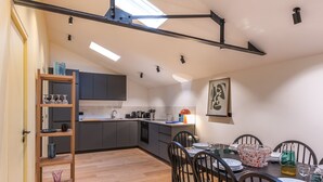 A modern kitchen with grey cabinets, a wooden dining table set for four, and a skylight above.