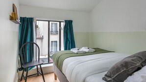 A bedroom with a bed, a chair, a window with curtains, and a view of a building outside.