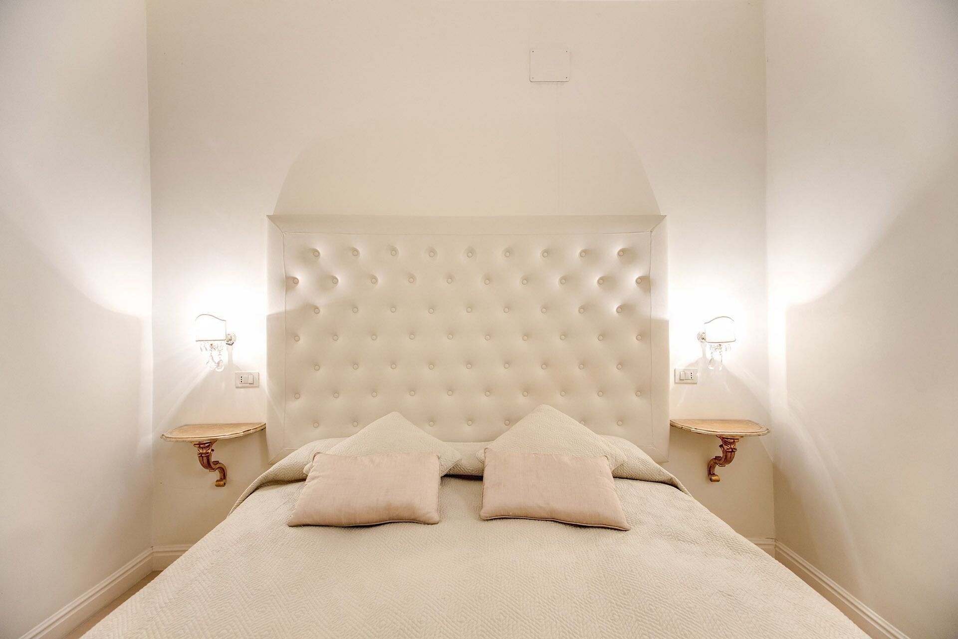 Ein Schlafzimmer mit einem gebürsteten Kopfende, zwei Nachttischen mit Lampen und einem Bett mit zwei Kissen.