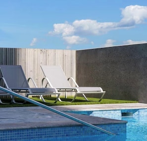 A swimming pool with two lounge chairs and a concrete wall.