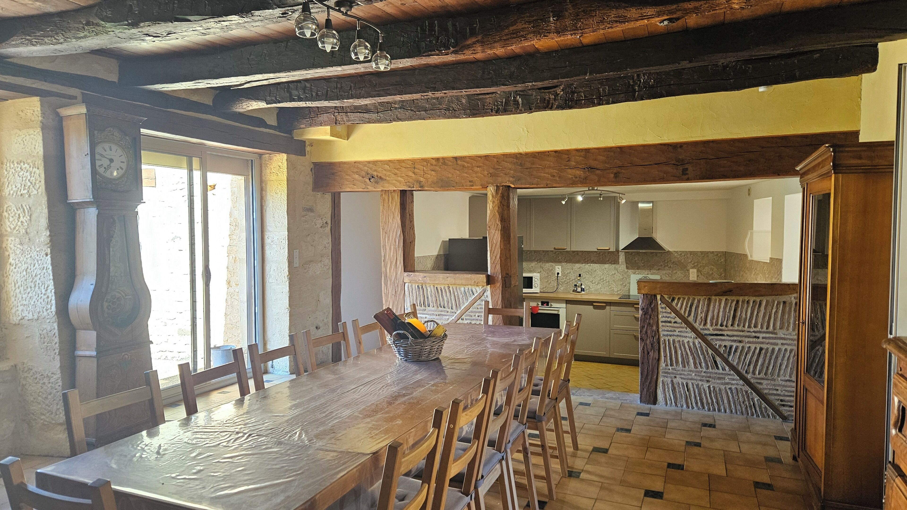 Un coin repas rustique avec une table et des chaises en bois, un panier rempli d’objets, et une cuisine en arrière-plan.