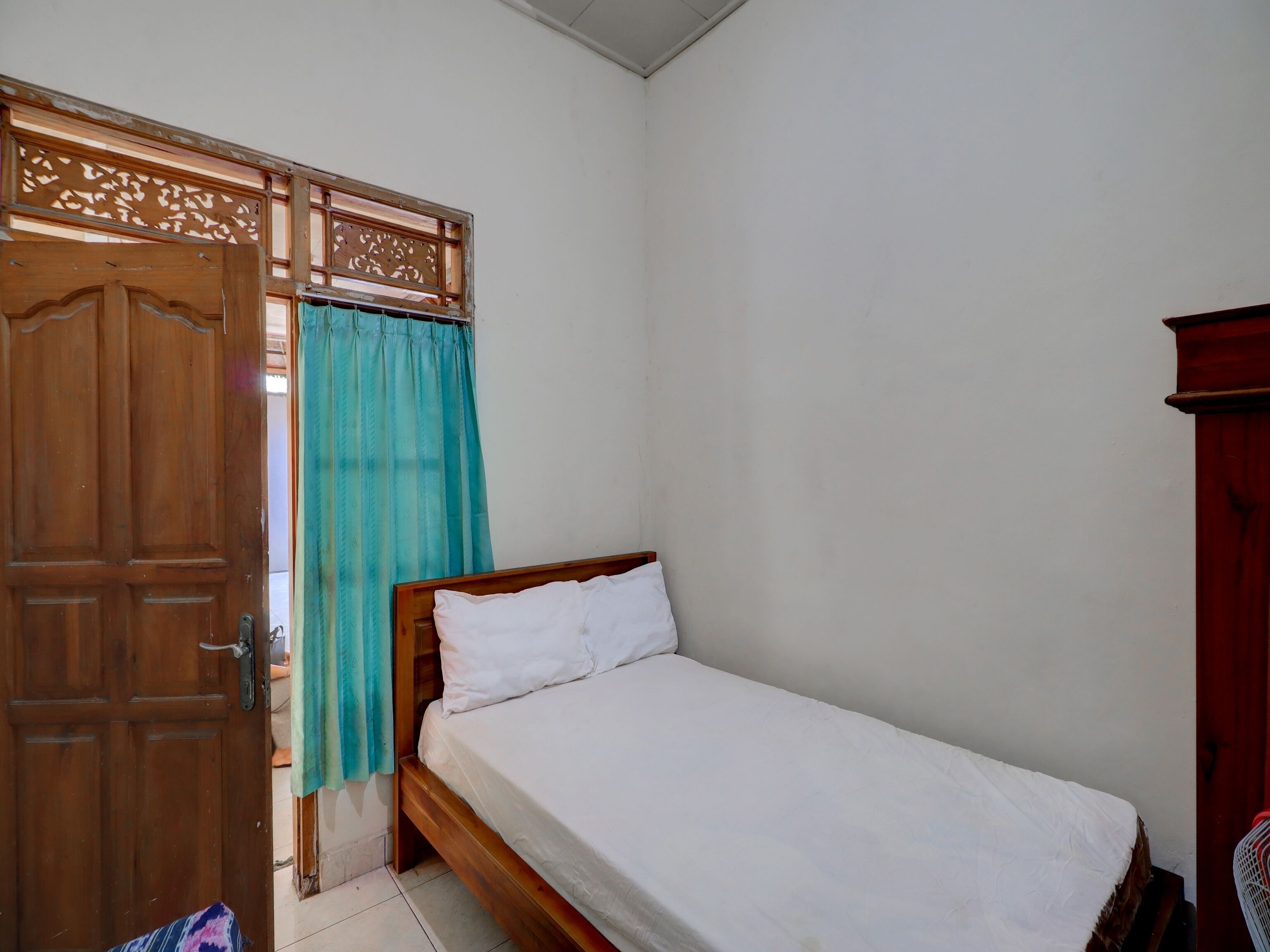 Una habitación pequeña y sencilla con una puerta de madera, una cama con ropa blanca y una cortina.