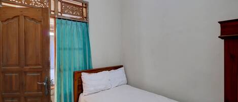 Una habitación pequeña y sencilla con una puerta de madera, una cama con ropa blanca y una cortina.