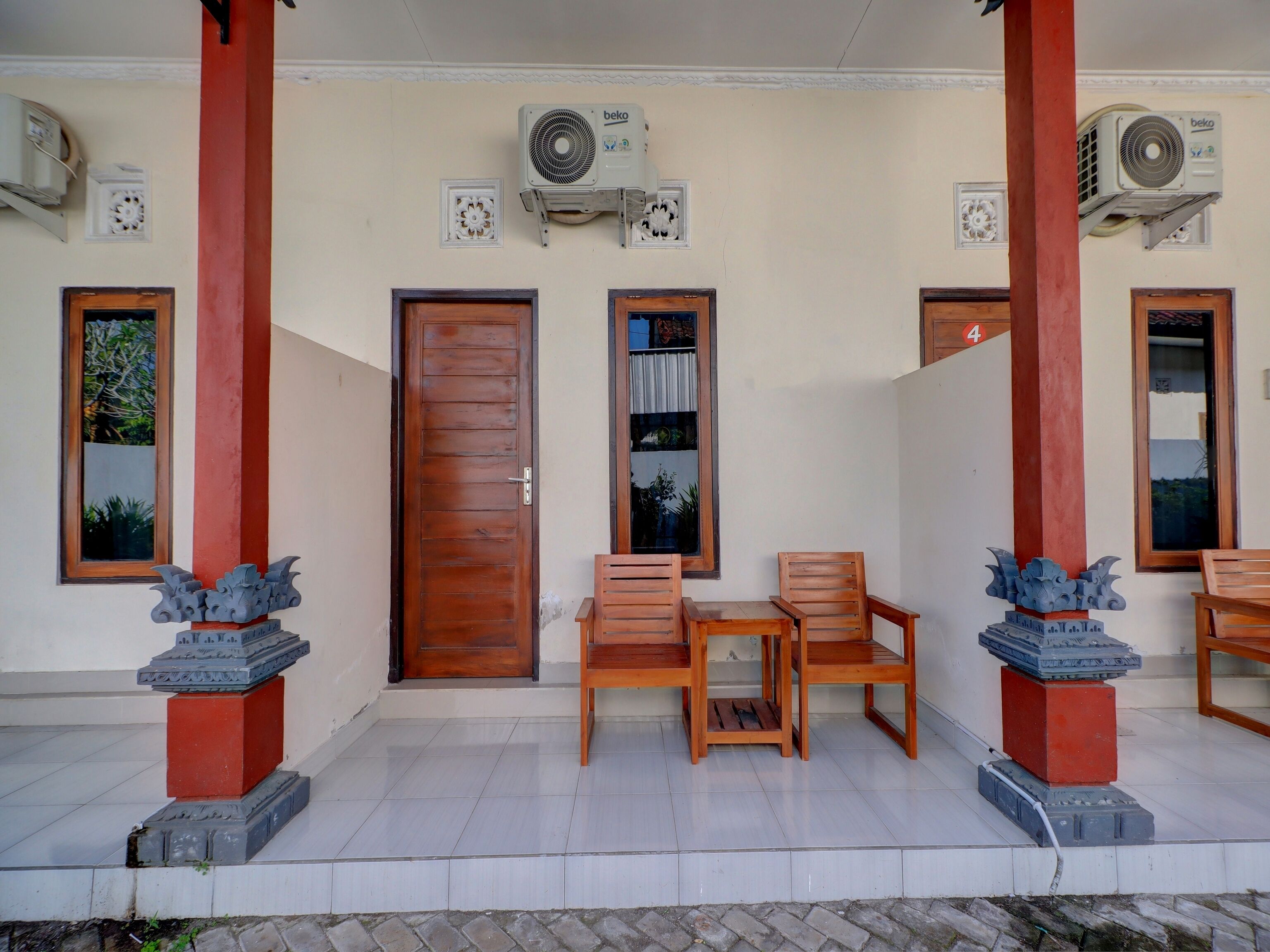 A covered outdoor area with a wooden door, two air conditioning units, and a small table with chairs.