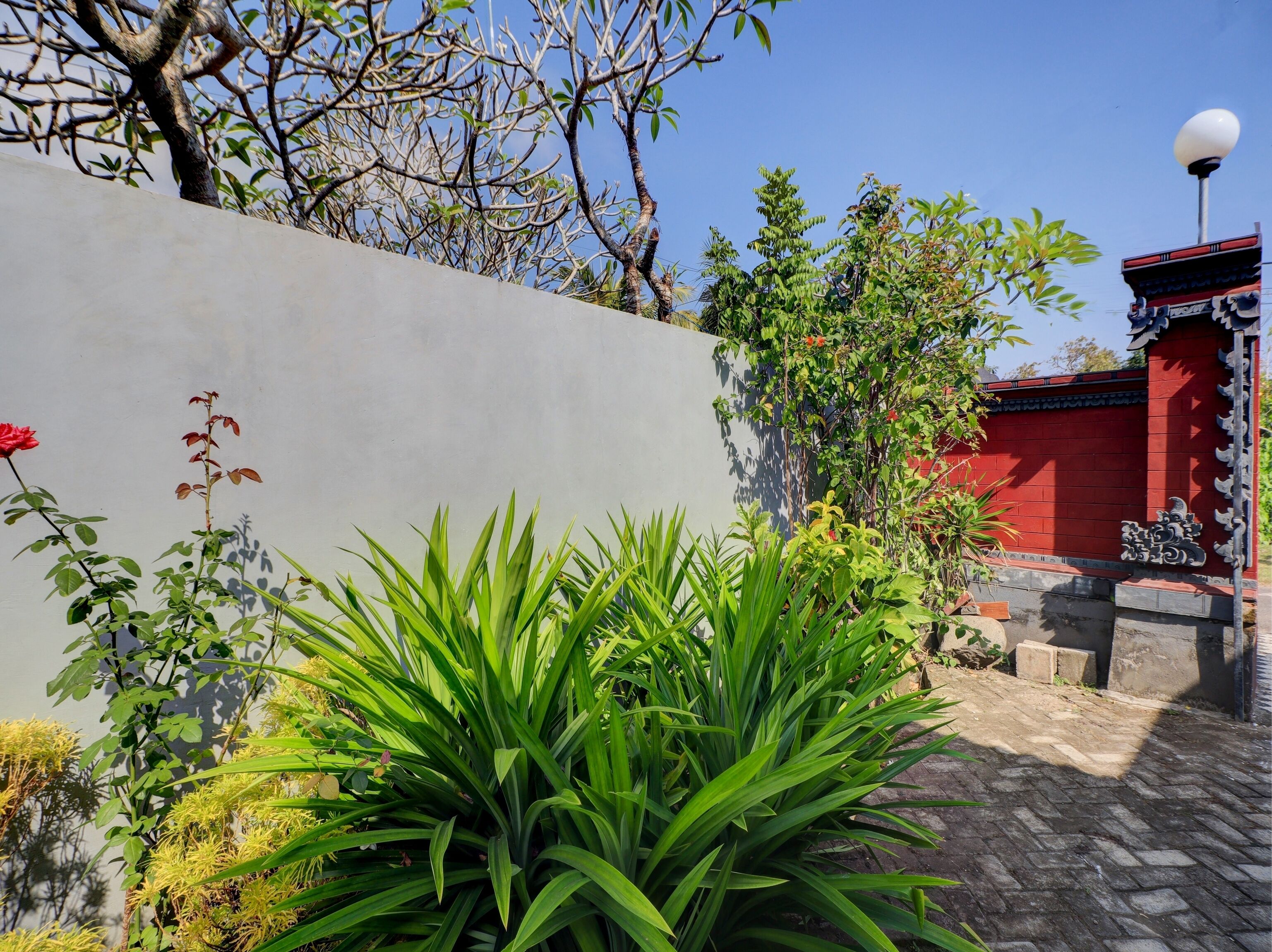 Un patio con pared gris, plantas verdes, un edificio rojo y un adorno decorativo tradicional.