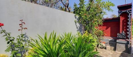 Un patio con pared gris, plantas verdes, un edificio rojo y un adorno decorativo tradicional.