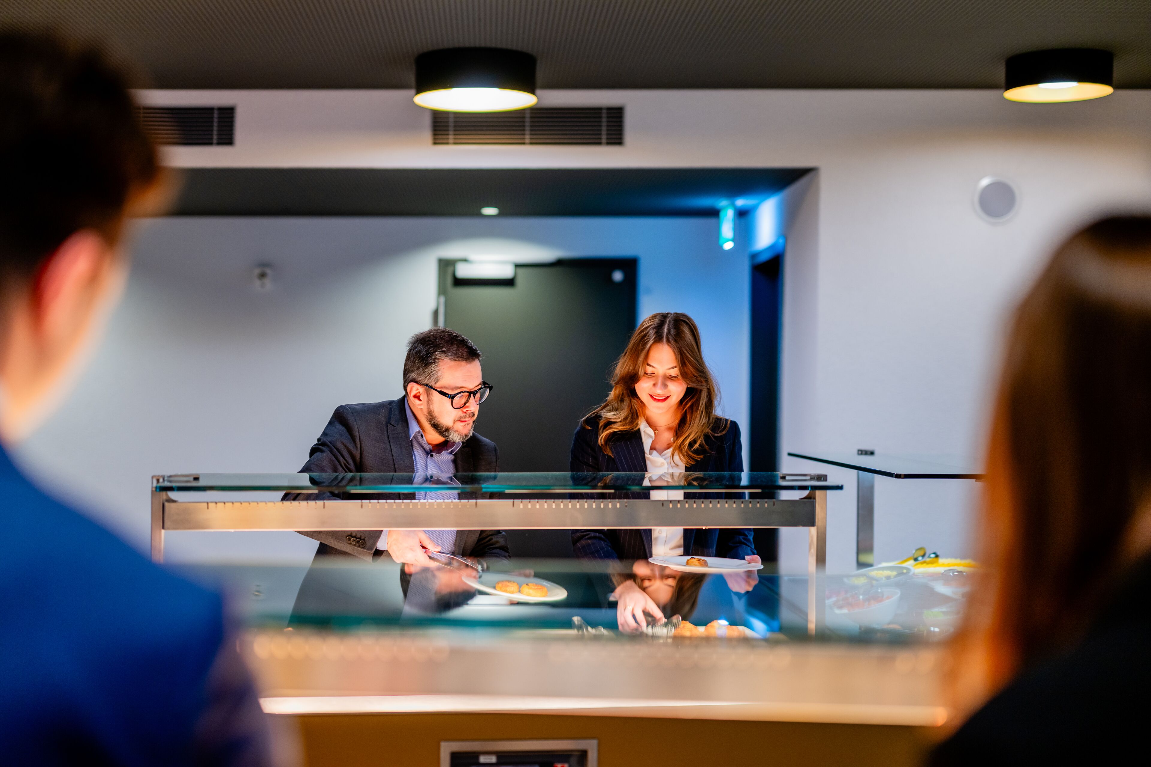 A modern hotel lobby with a reception desk, a glass partition, and a door in the background.