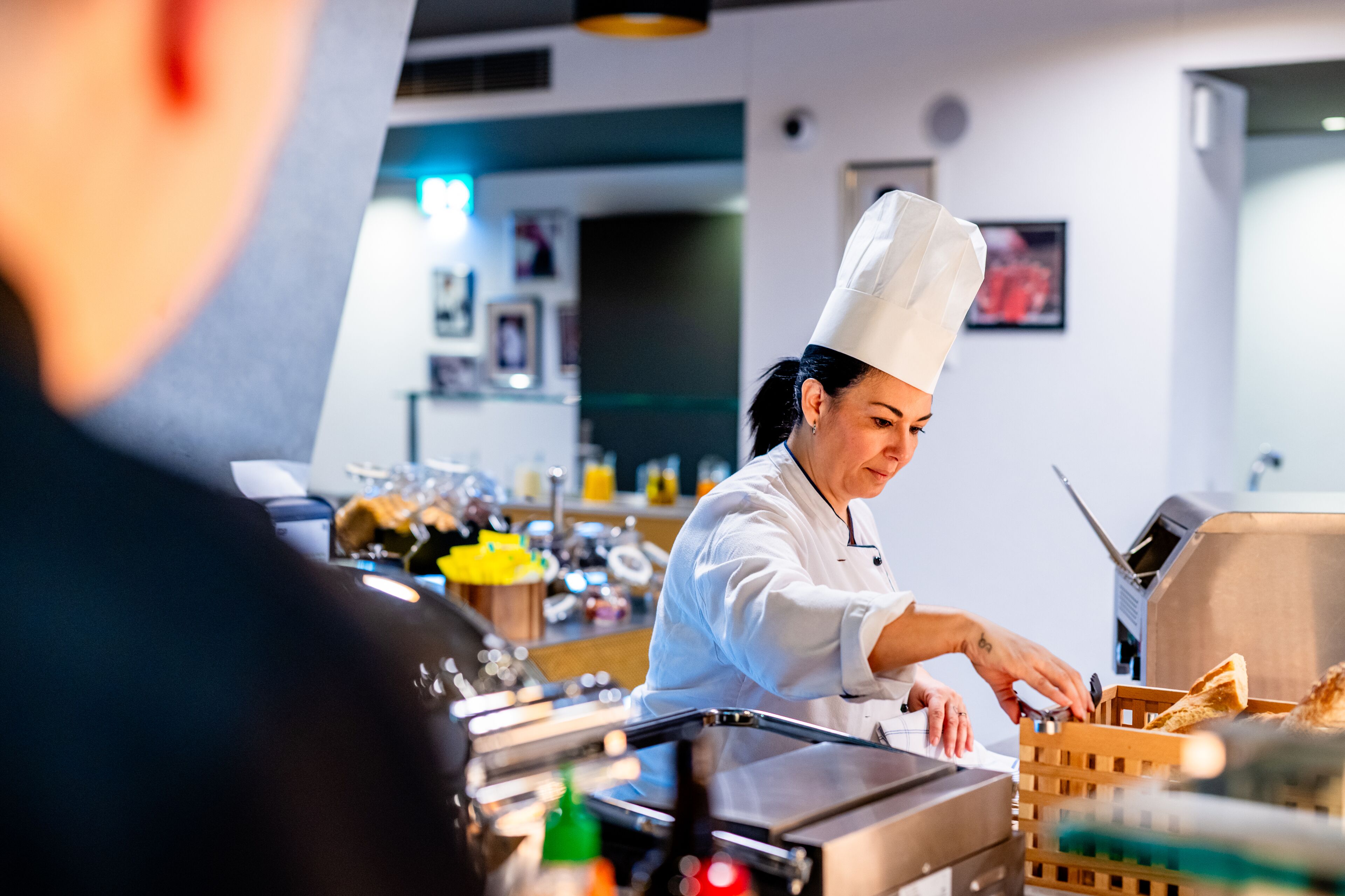 A chef in a white uniform preparing food in a kitchen with various cooking equipment and ingredients visible.
