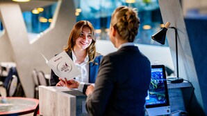 A reception desk with a digital screen displaying a scenic view, a modern interior with geometric wall designs, and a well-lit environment. - The Freddie Mercury Hotel (Montreux)