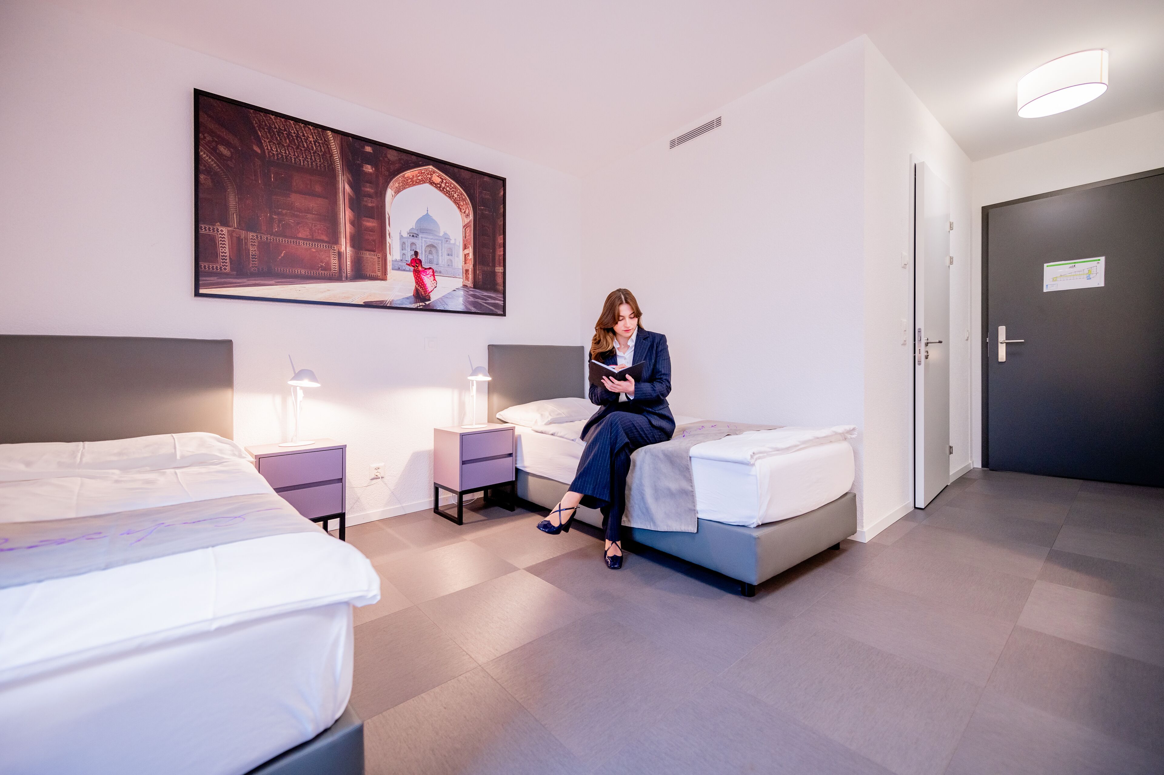 Ein Hotelzimmer mit zwei Betten, einem Nachttisch, einer Lampe und einem großen gerahmten Bild an der Wand.
