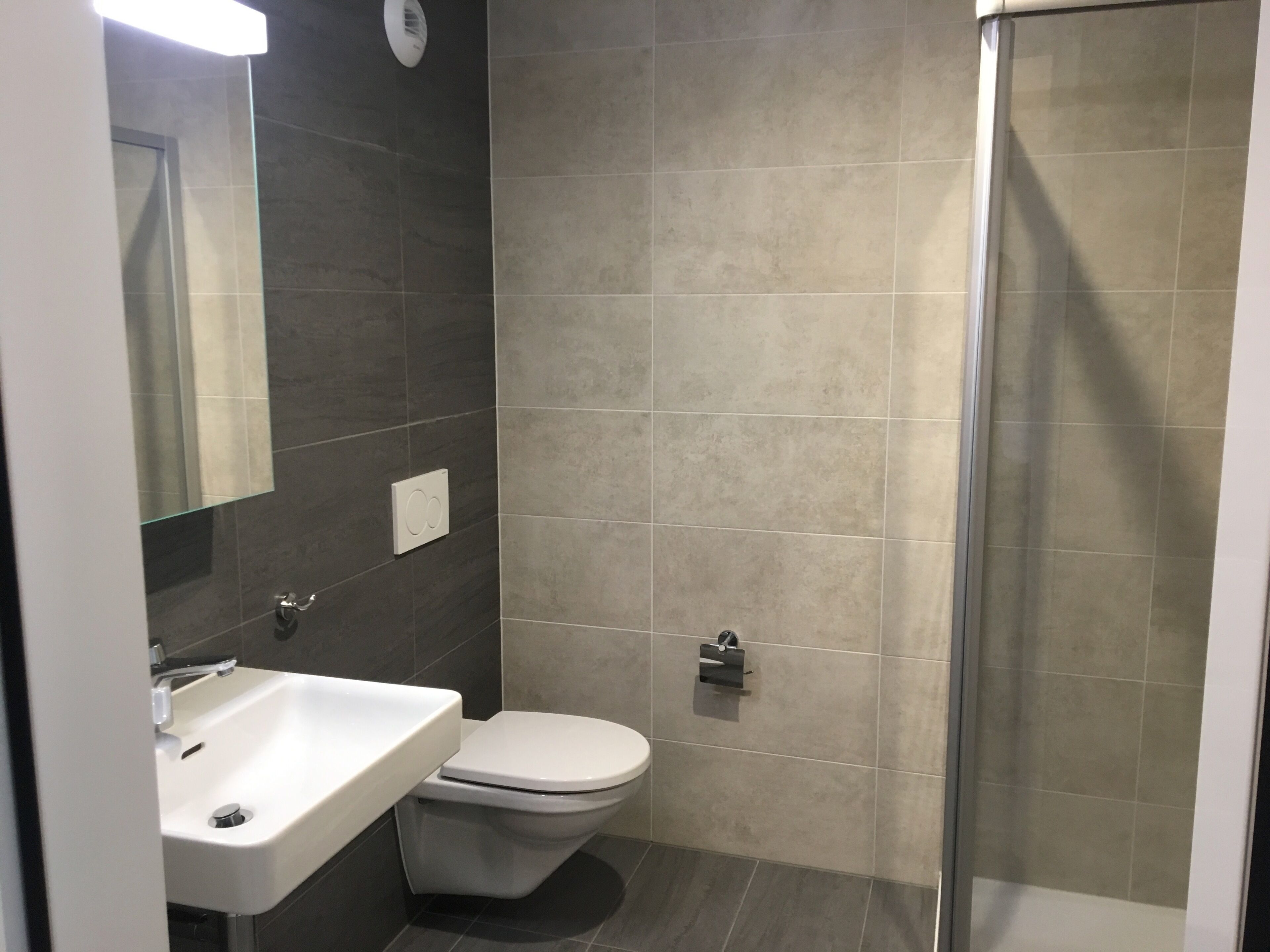 Een badkamer met een wit wastafelmeubel, een toilet en een douchecabine met glazen wanden.