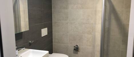 Een badkamer met een wit wastafelmeubel, een toilet en een douchecabine met glazen wanden.
