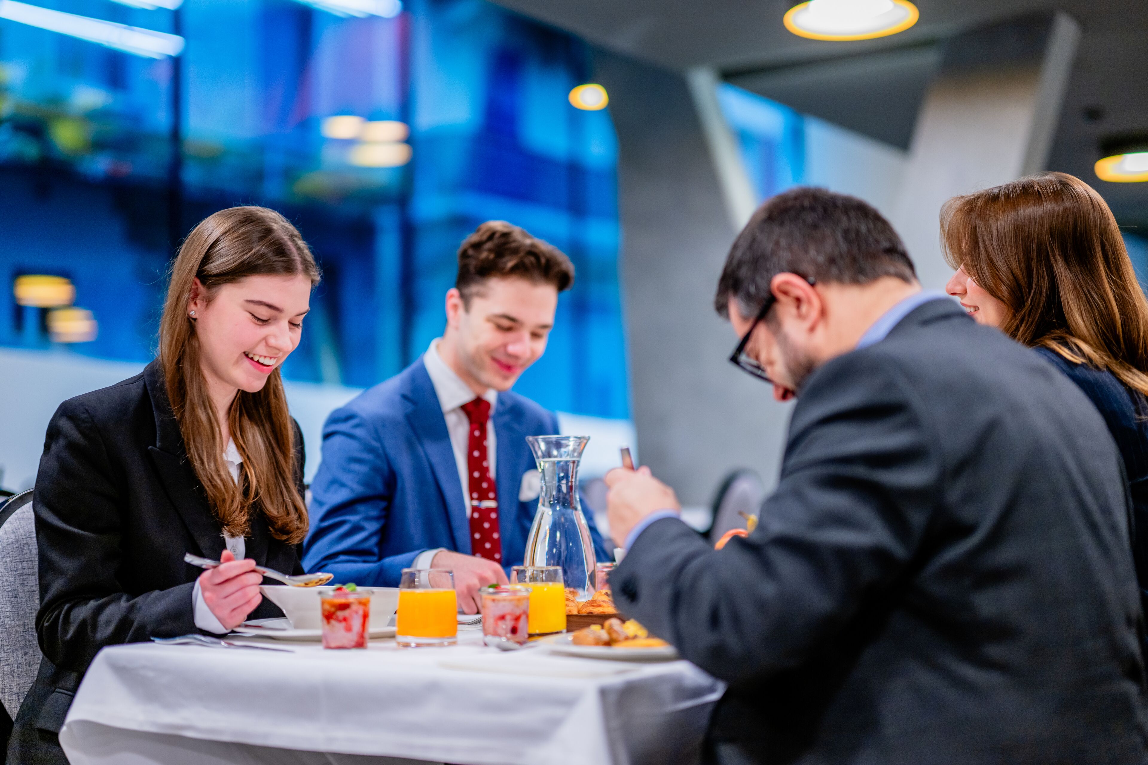 Un grupo de personas cenando en una mesa en un espacio interior moderno con paredes de vidrio.