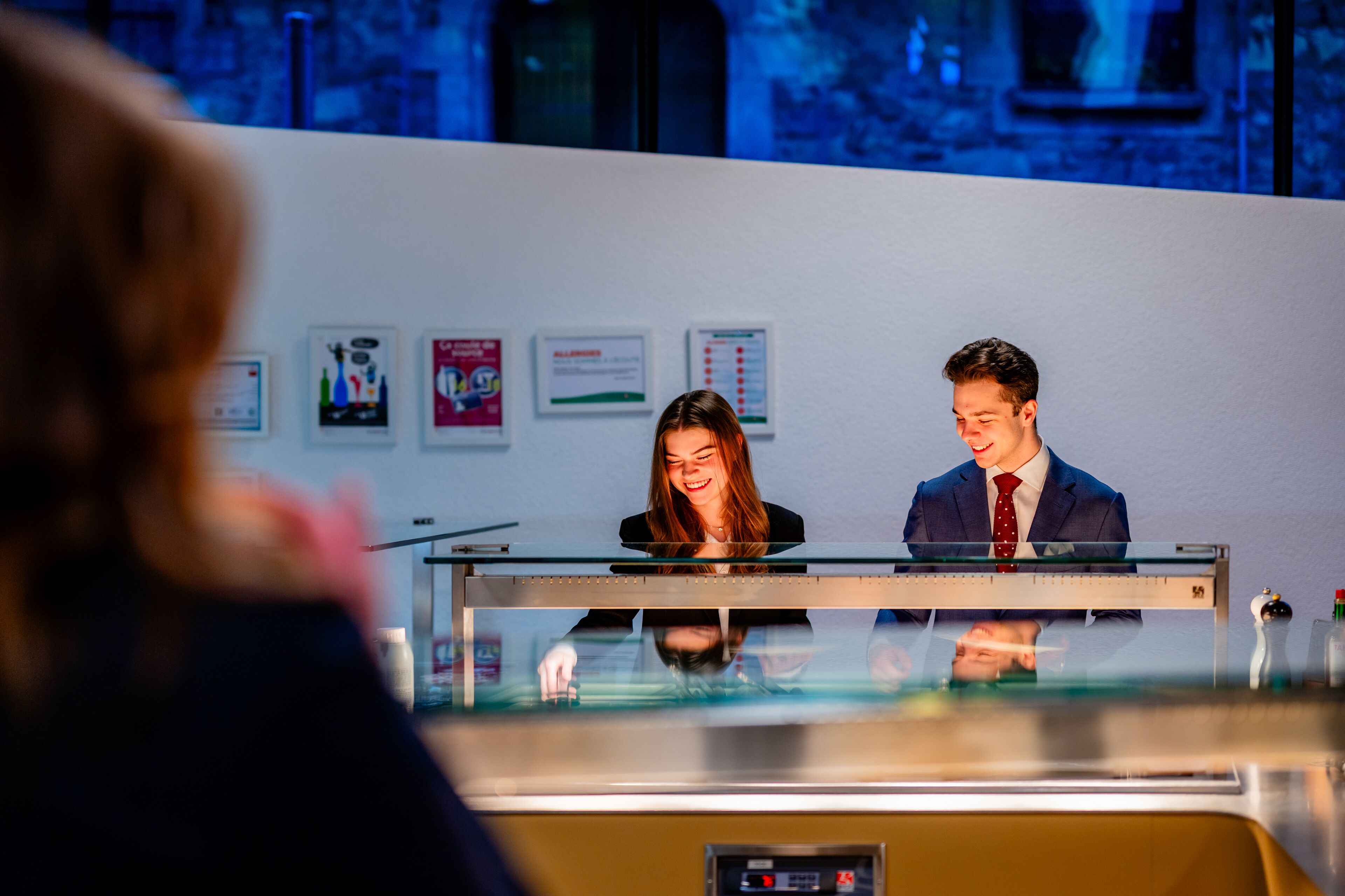 A reception desk with two staff members, a glass partition, and framed informational posters on the wall.