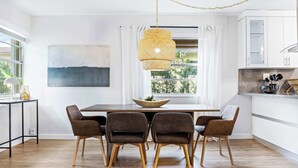 A modern dining area with a wooden table, four chairs, a hanging light fixture, and a window with curtains.