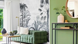 A room with a green sofa, a round table, a wall mural, and a mirror.