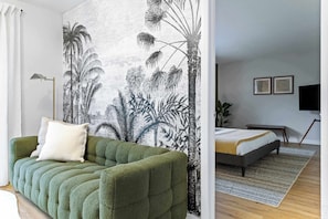 A room with a green sofa, a bed with a white and yellow bedspread, a large wall tapestry, a floor lamp, and a television mounted on the wall. - Hidden Garden, Miami Escape, Parking and Spacious (Cutler Bay)