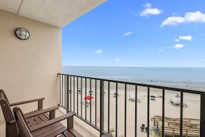 A balcony with a view of a beach, a wooden bench, and a railing.