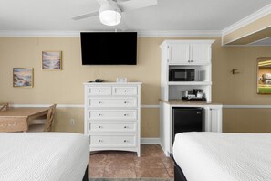 A hotel room with two beds, a TV, a kitchenette, and a ceiling fan.