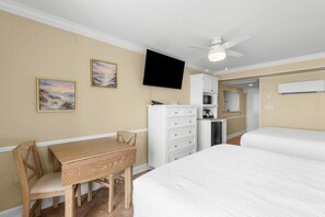 A hotel room with a bed, a desk, a chair, a television, a ceiling fan, and a kitchenette.