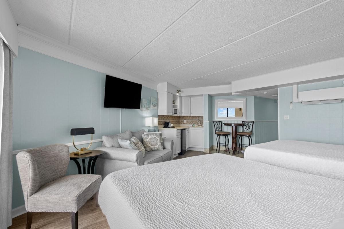 Habitación de hotel con una cama grande, un escritorio, una silla, un televisor montado en la pared y una zona de kitchenette.
