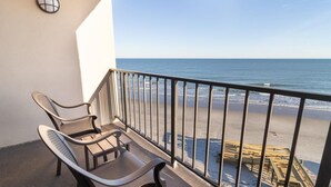 A balcony with two chairs and a small table, overlooking a beach with wooden structures and the ocean. - Beach Bliss Haven 6th Floor (Pawleys Island)