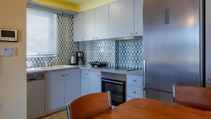 Cocina compacta con armarios grises, un refrigerador de acero inoxidable, horno empotrado y cafetera sobre la encimera.