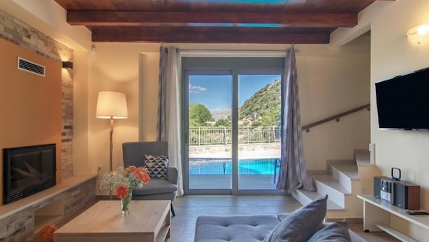 Una sala de estar con chimenea, sofá, mesa de centro y vistas a una piscina y montañas.