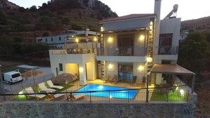 Una casa moderna de dos pisos con piscina, paredes de piedra e iluminación exterior.