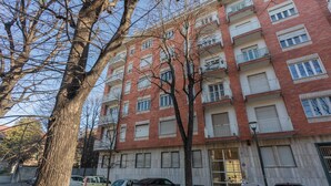 A multi-story brick building with balconies, parked cars, and a tree in the foreground. - Monte Grappa Apartment by Wonderful Italy (Turin)