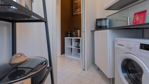 A compact kitchen with a washing machine, a coffee machine, and a small cabinet. - Monte Grappa Apartment by Wonderful Italy (Turin)