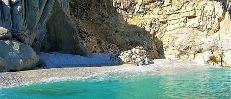 A coastal scene with clear turquoise water, rocky cliffs, and a pebble beach.