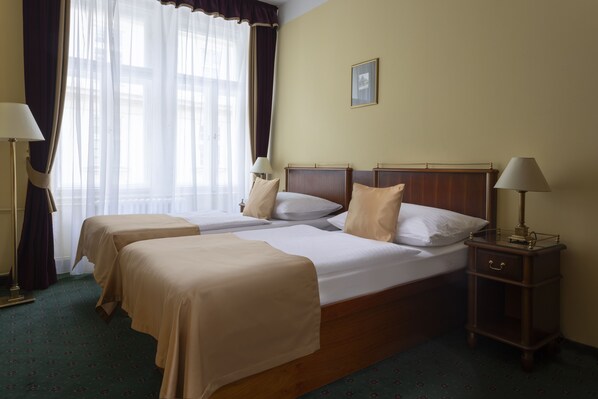 A hotel room with two beds, a nightstand, a lamp, and a window with curtains.