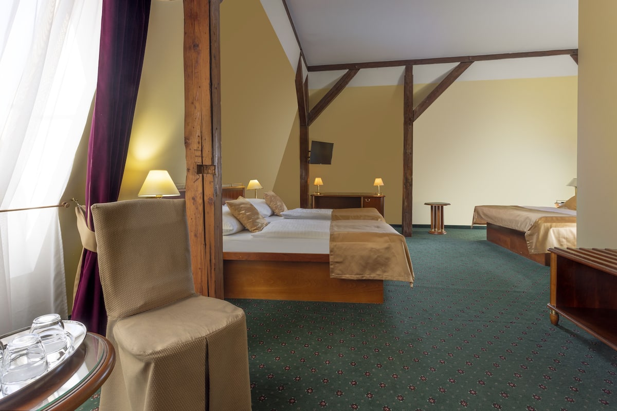 A hotel room with a bed, a chair, a table with glasses, and a TV on the wall.