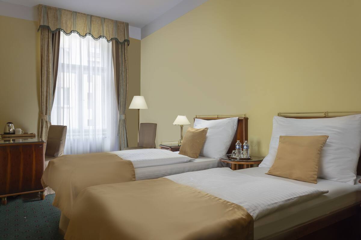 A hotel room with two beds, a desk, a chair, a lamp, and a window with curtains.