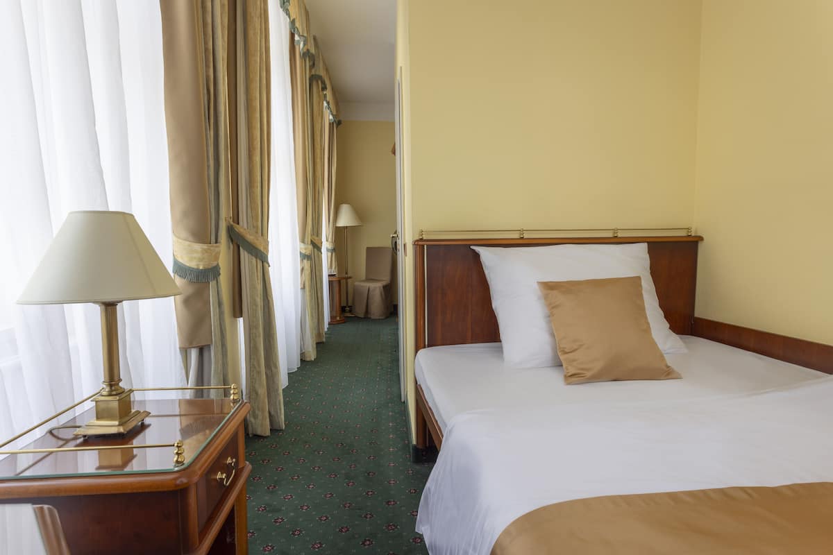 A hotel room with a bed, a nightstand with a lamp, a wooden headboard, and a carpeted floor.